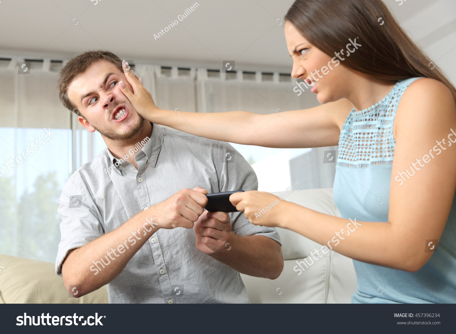 Couple or friends fighting for a mobile phone sitting on a couch at home #457396234