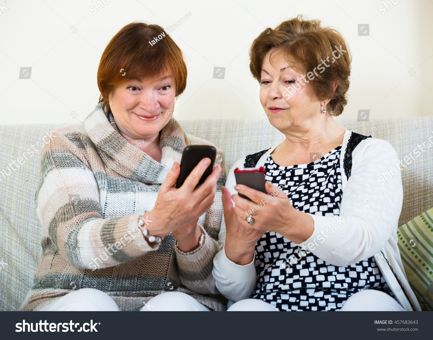 Smiling elderly friends sitting with smartphones in living room #457683643