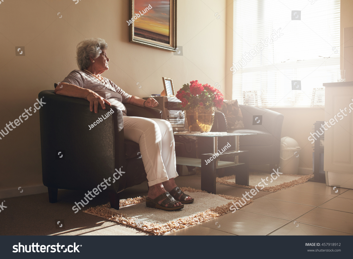 Senior woman sitting alone on a chair at home. Retired woman relaxing in living room. #457918912