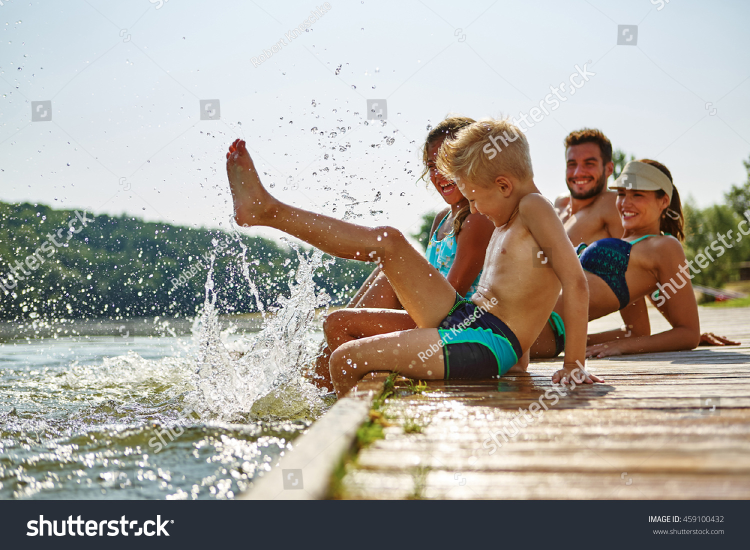Family bathing and splashing water with their foot at a lake in summer #459100432
