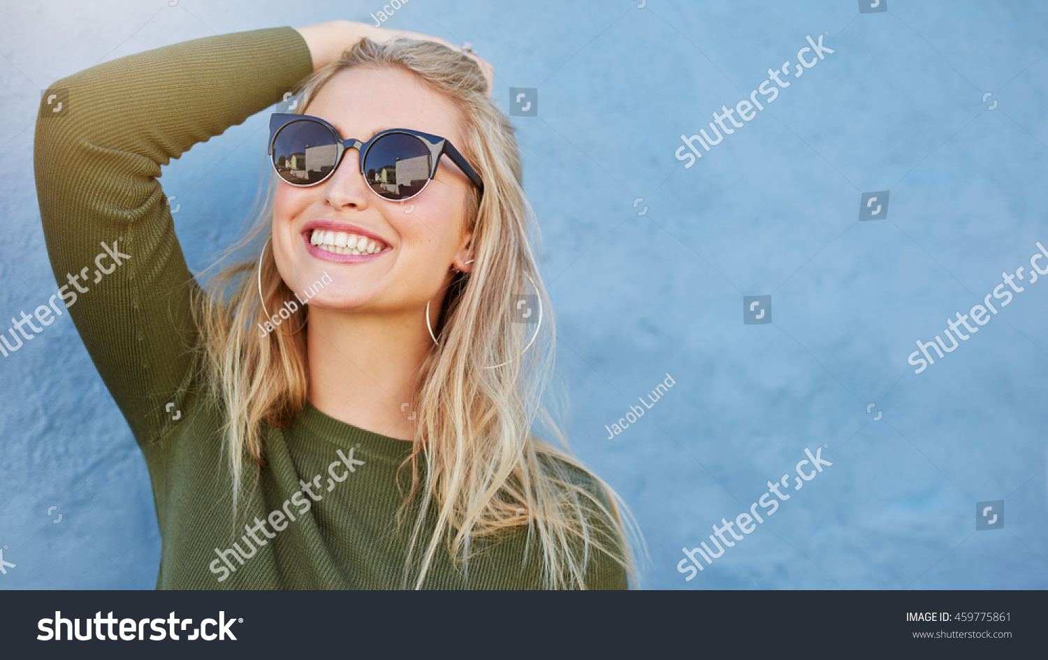 Close up shot of stylish young woman in sunglasses smiling against blue background. Beautiful female model with copy space. #459775861