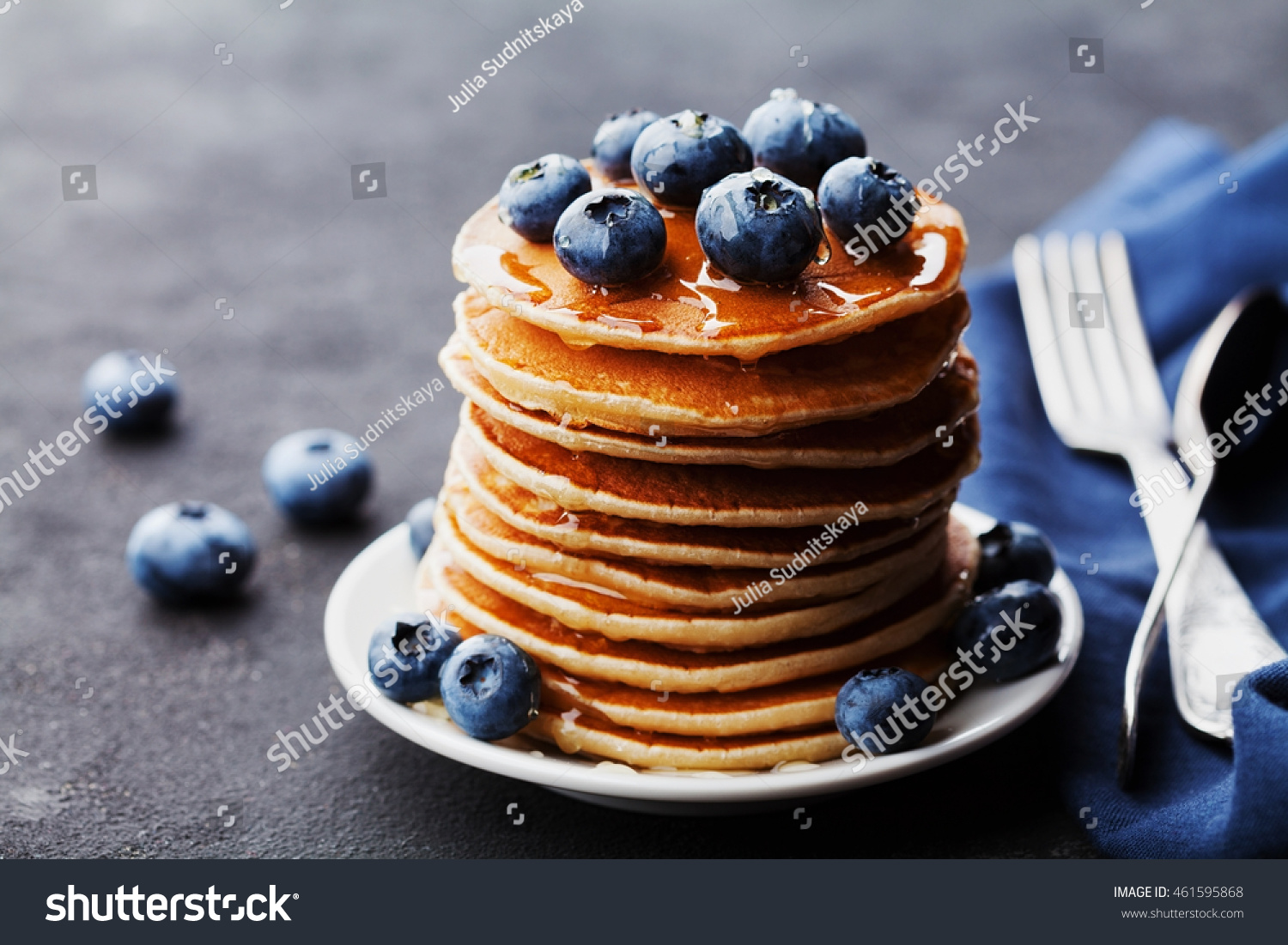Stack of baked american pancakes or fritters with blueberries and honey syrup on rustic black table. Delicious dessert for breakfast. #461595868