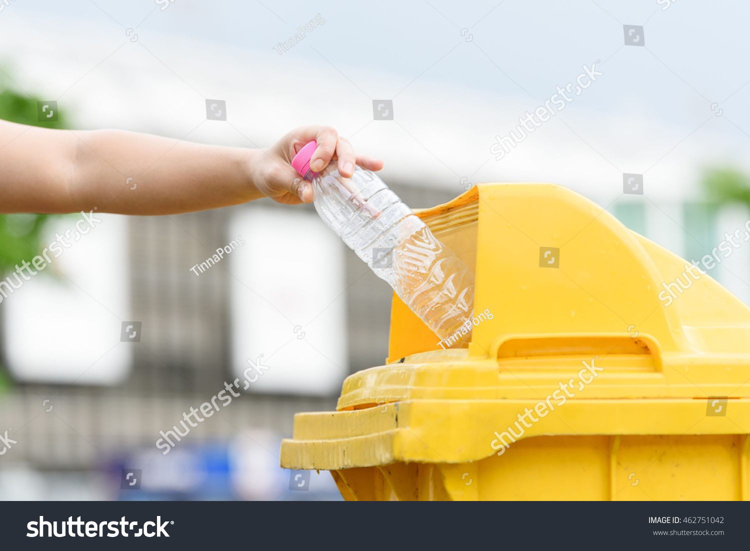 Selective focus on hand dropping empty plastic bottle to the yellow garbage bin. #462751042