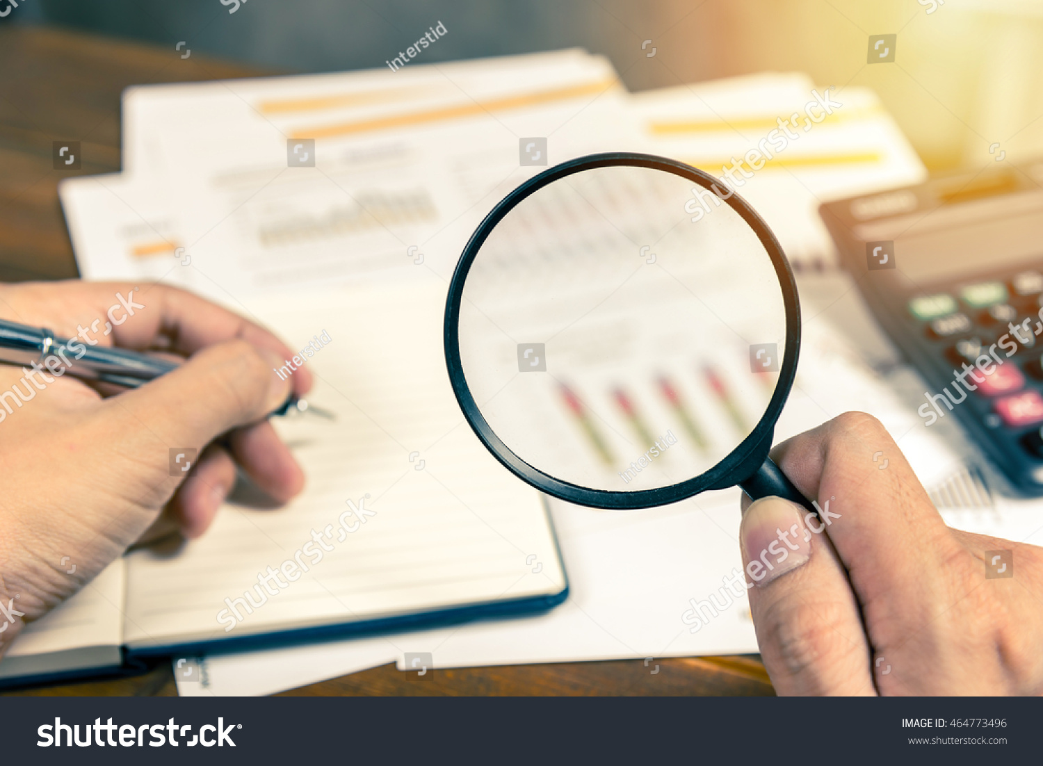 Man hand holding magnifying glass analyzing business financial data. Photo with sunlight filter effect. #464773496