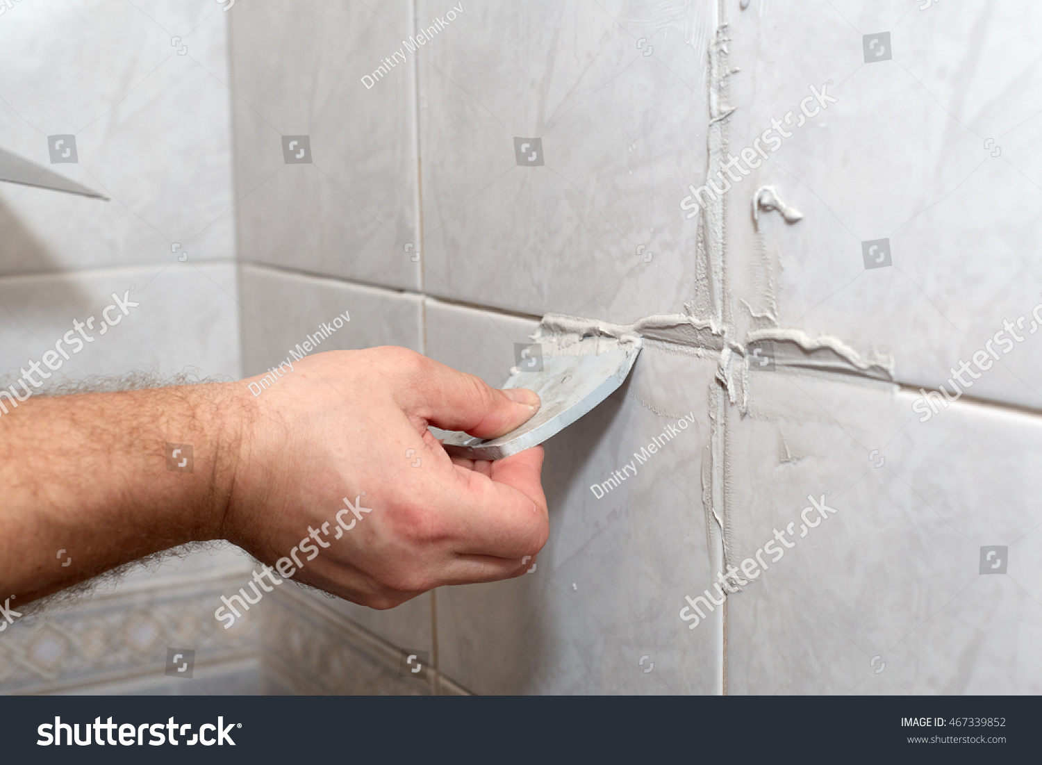 The male hand with the rubber spatula applies grout on a seam between tiles in a bathroom. Home repairs. #467339852