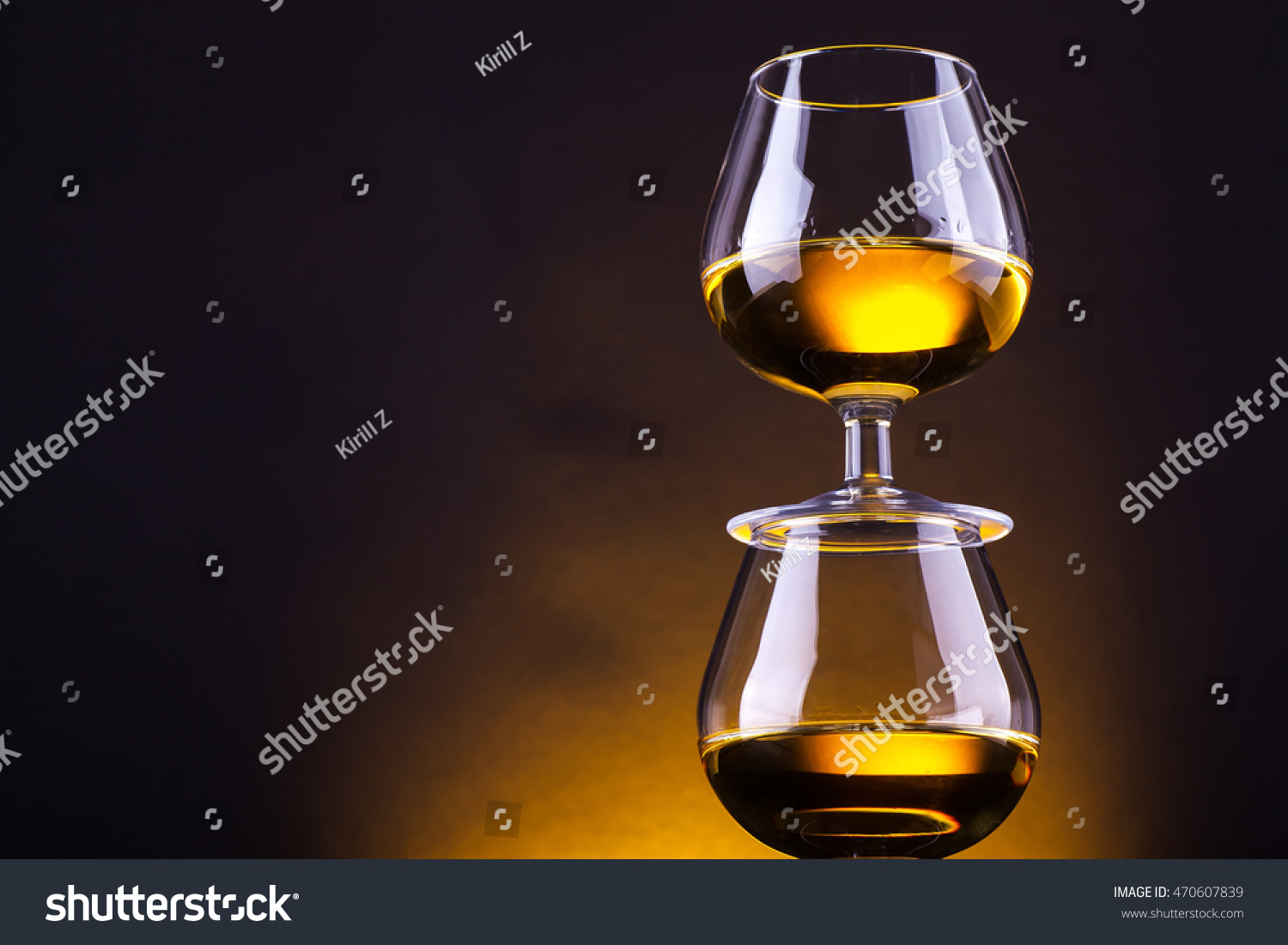 Snifter glasses with brandy stacked on top of each other over a yellow lit background #470607839