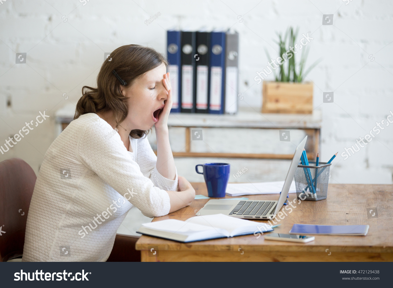 Portrait of young woman sitting at table in front of laptop, sleepy, tired, overworked, lazy to work. Attractive business woman yawning in home office relaxing or bored after work on laptop computer #472129438