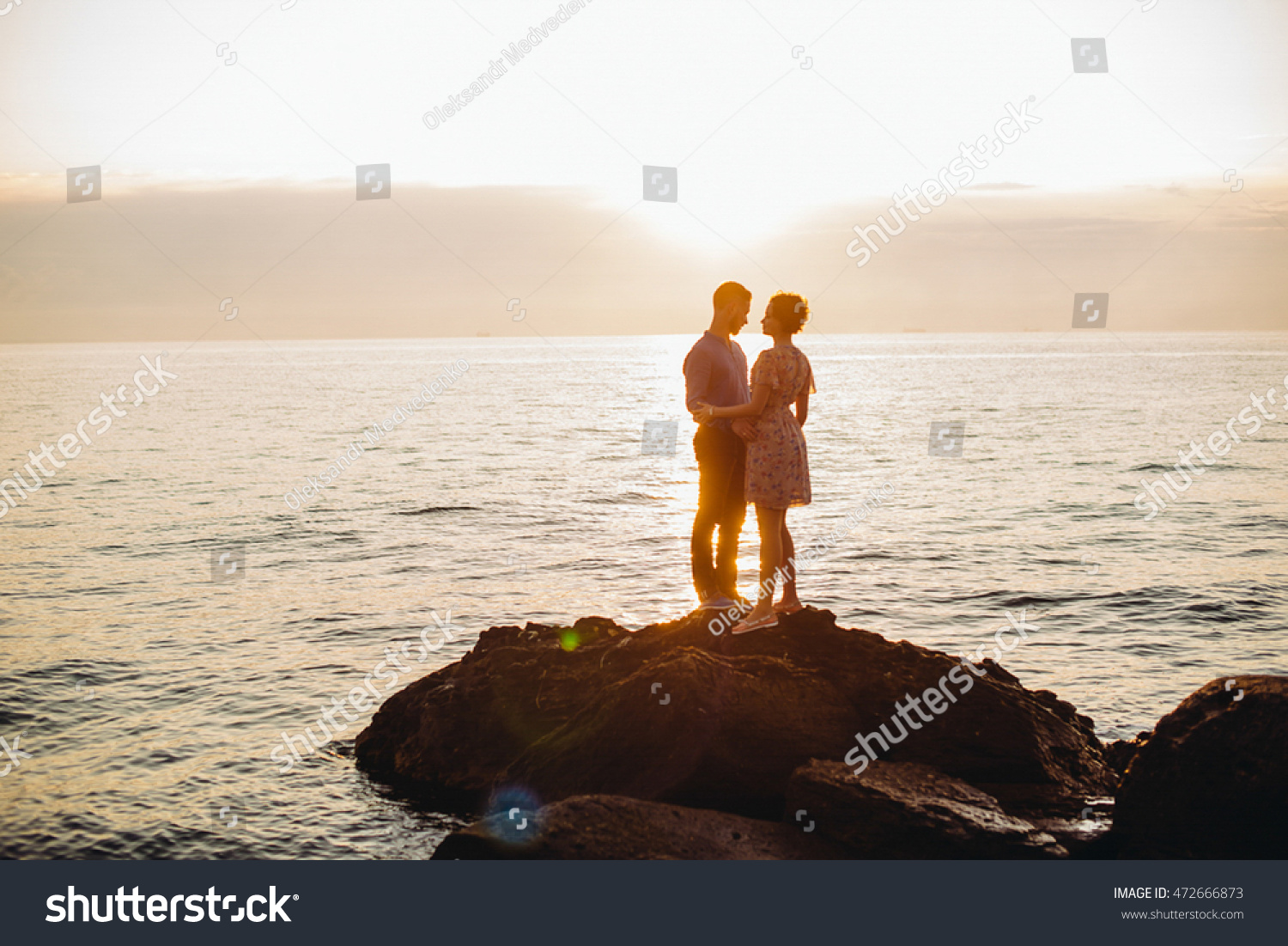 Bright evening sun shines over the couple posing on the stones by the calm sea #472666873