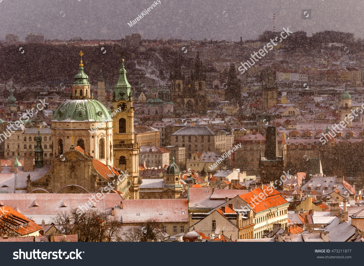 Amazing Gothic church of Our Lady and St. Nicolas church during winter day with heavy snow storm and sun rays peeping through clouds, Prague, Czech republic #473211877