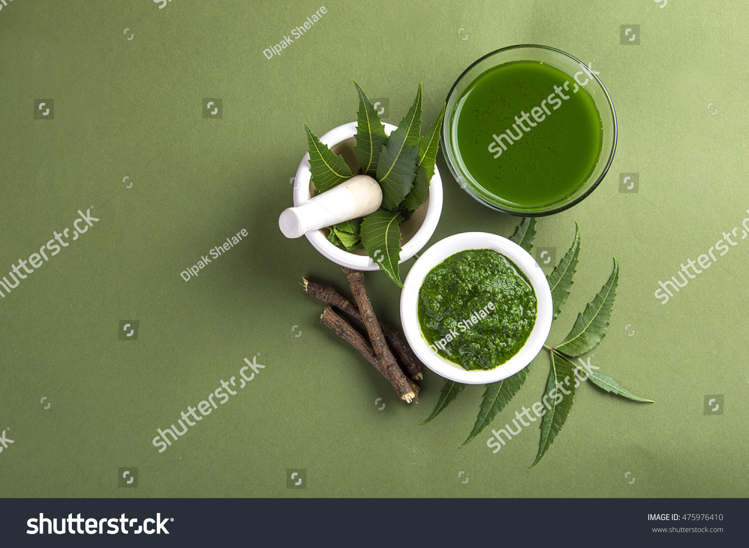 Medicinal Neem leaves in mortar and pestle with neem paste, juice and twigs on green background #475976410