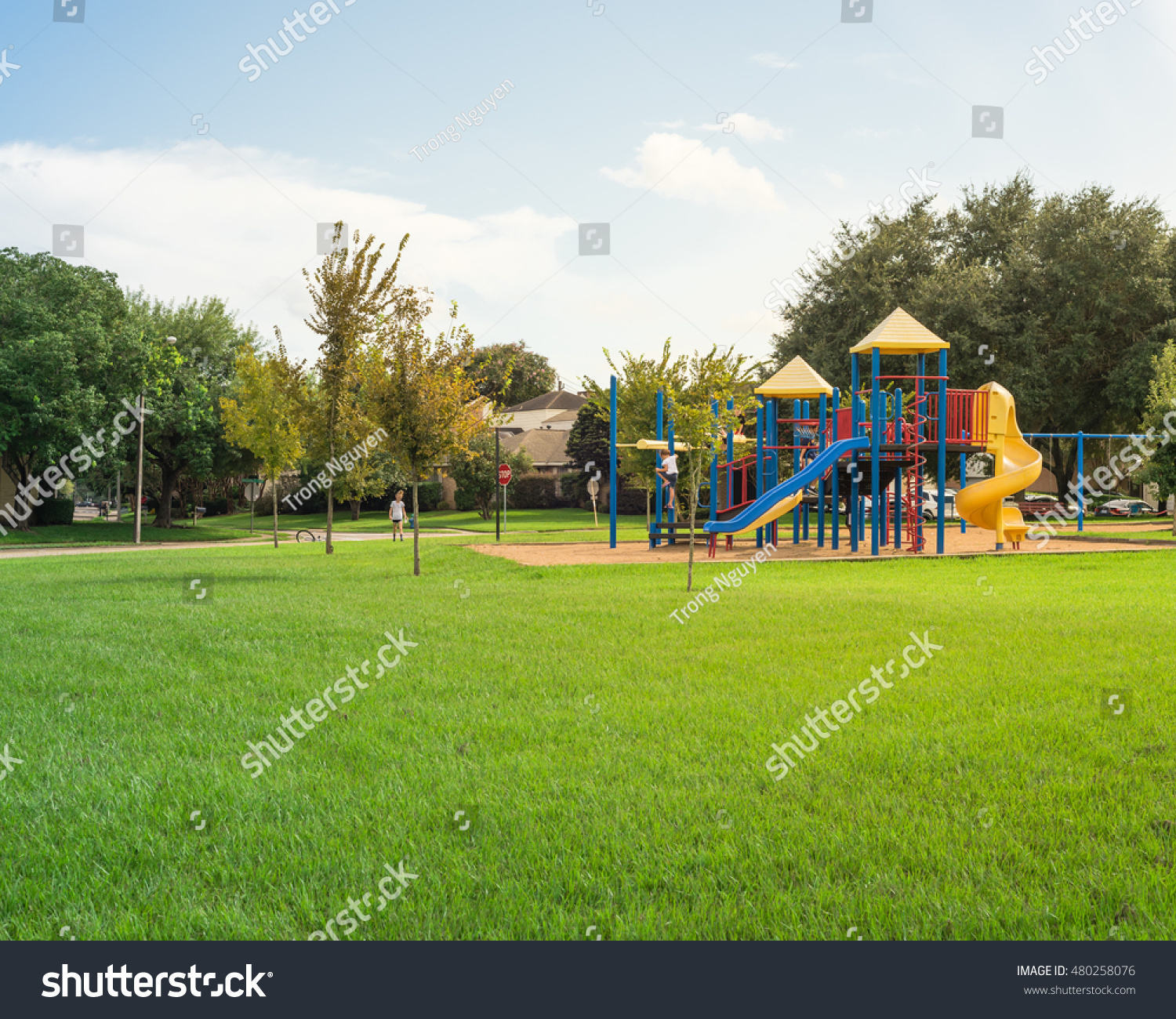Colorful children playground activities in public park surrounded by green trees at sunset in Houston, Texas. Children run, slide, swing on modern playground. Urban neighborhood childhood concept. #480258076