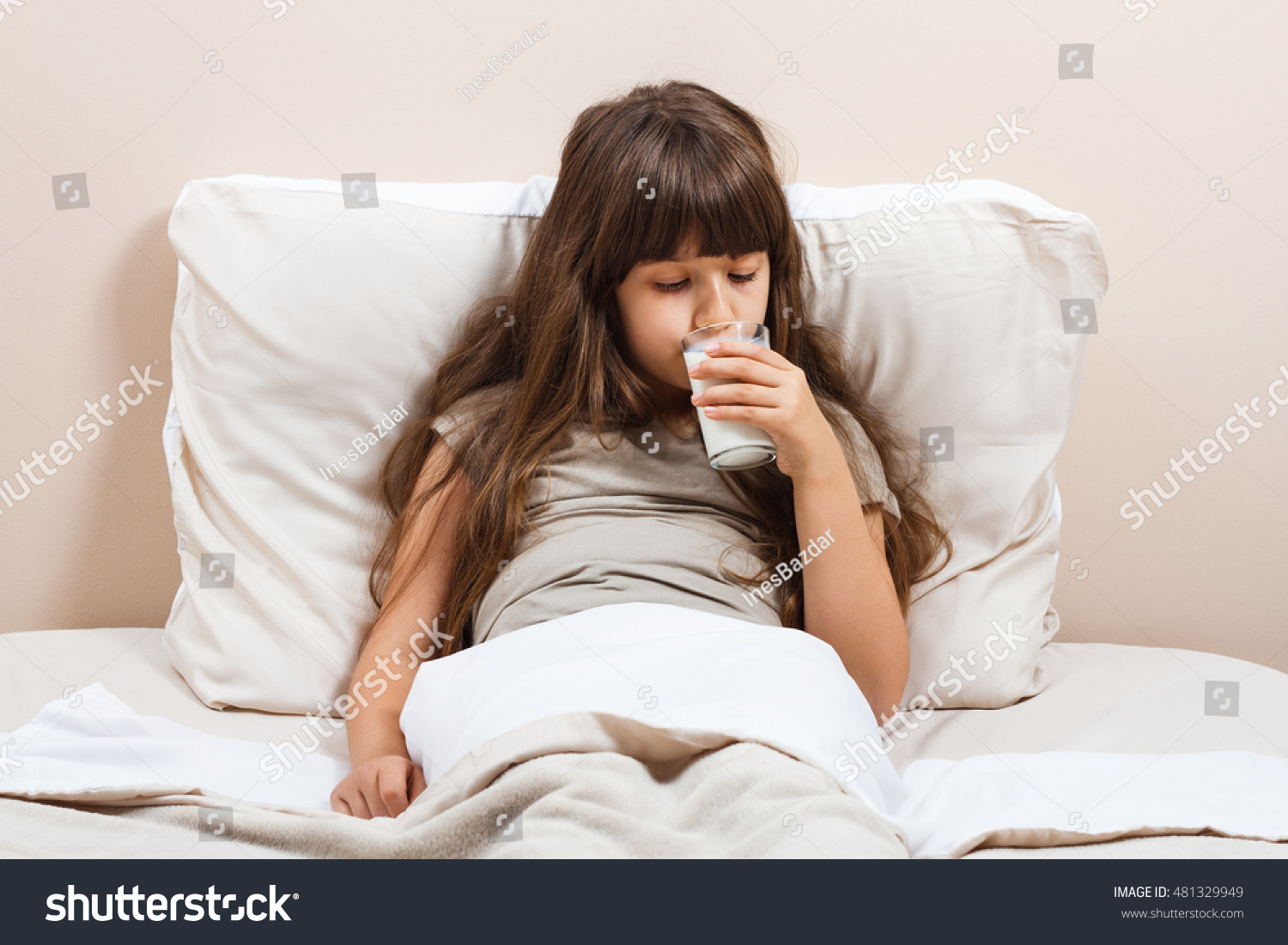 Cute little girl in pajamas is sitting on bed and drinking milk.Little girl drinking milk
 #481329949