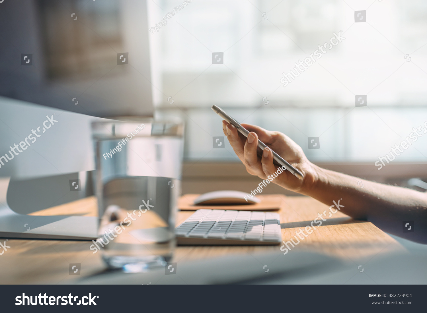 Female hands holding modern smartphone at office interior, Woman working at office and using smartphone, workspace manager in the early morning, Workplace in the early morning, Shallow DOF. #482229904