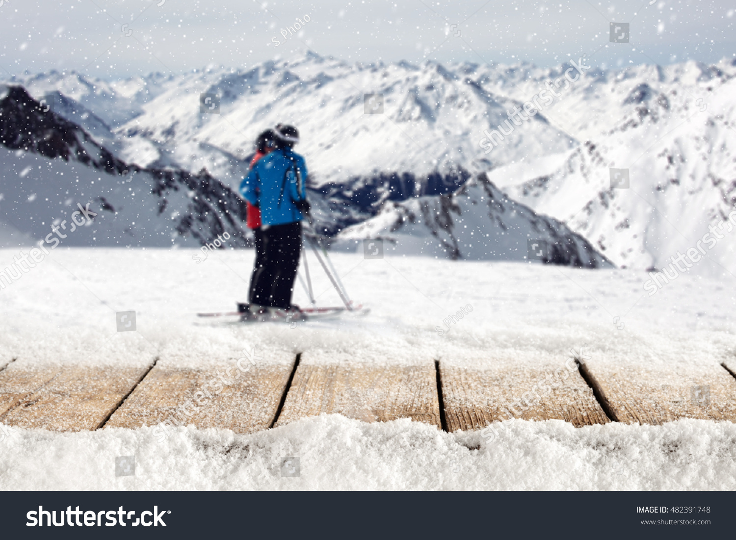 wooden table full of snow flakes and landscape of Alps with skier  #482391748