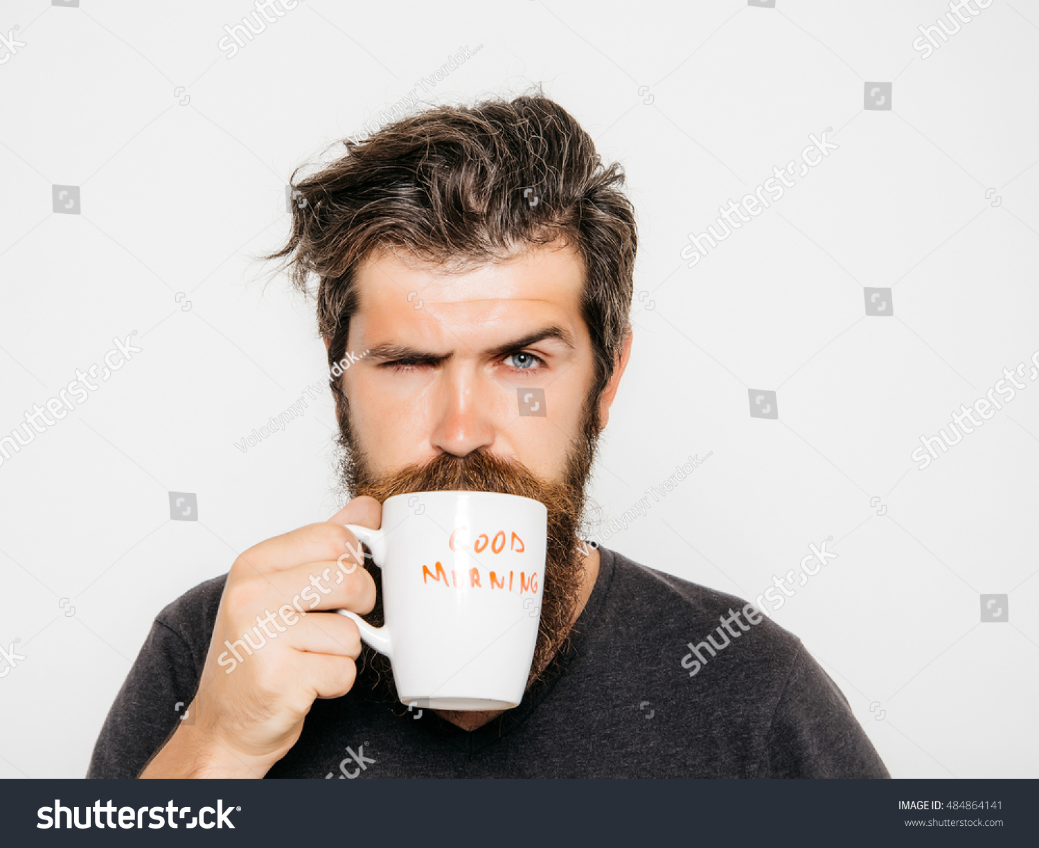 handsome bearded man with stylish hair beard and mustache on serious face in shirt holding white cup or mug with good morning text drinking tea or coffee in studio on grey background #484864141
