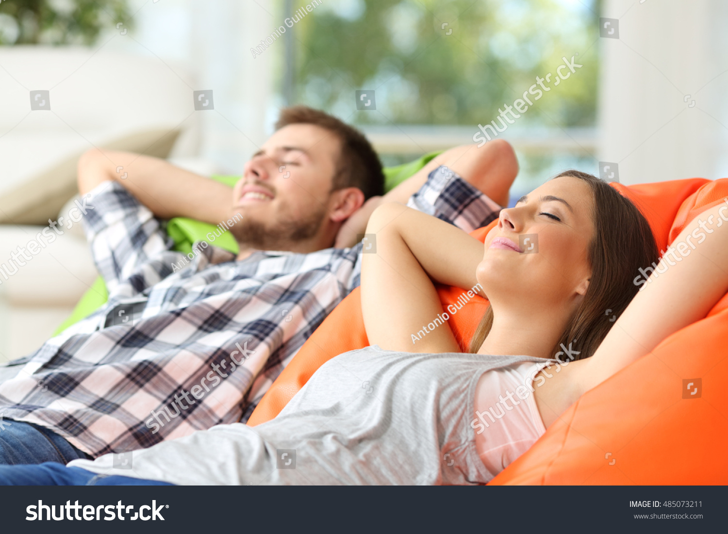 Couple or roommates relaxing lying on comfortable poufs in the living room at home #485073211