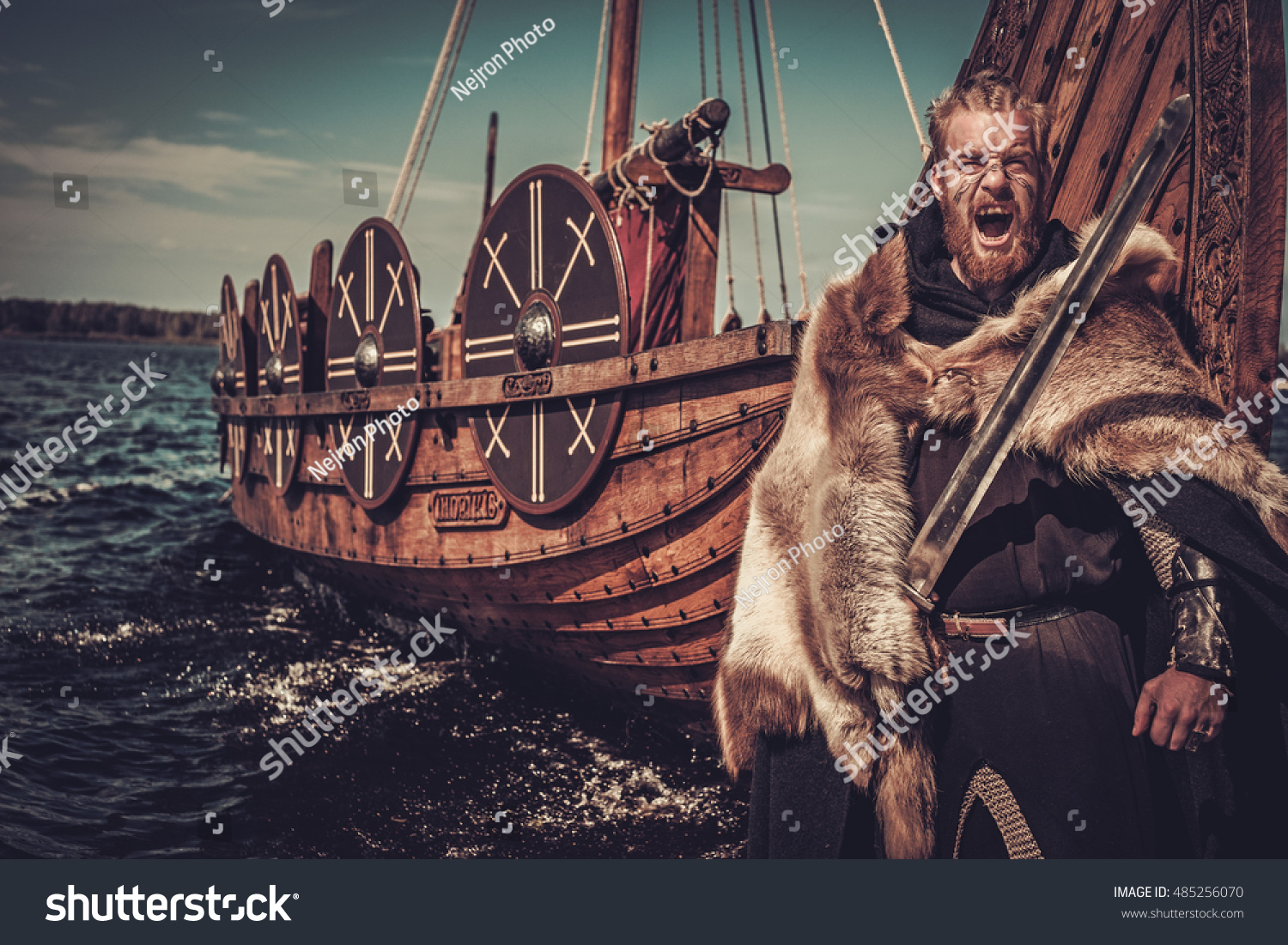 Viking warrior with sword and shield standing near Drakkar on the seashore. #485256070