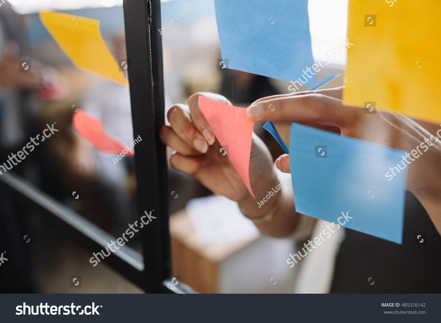 Close up shot of hands of woman sticking adhesive notes on glass wall in office #485376142
