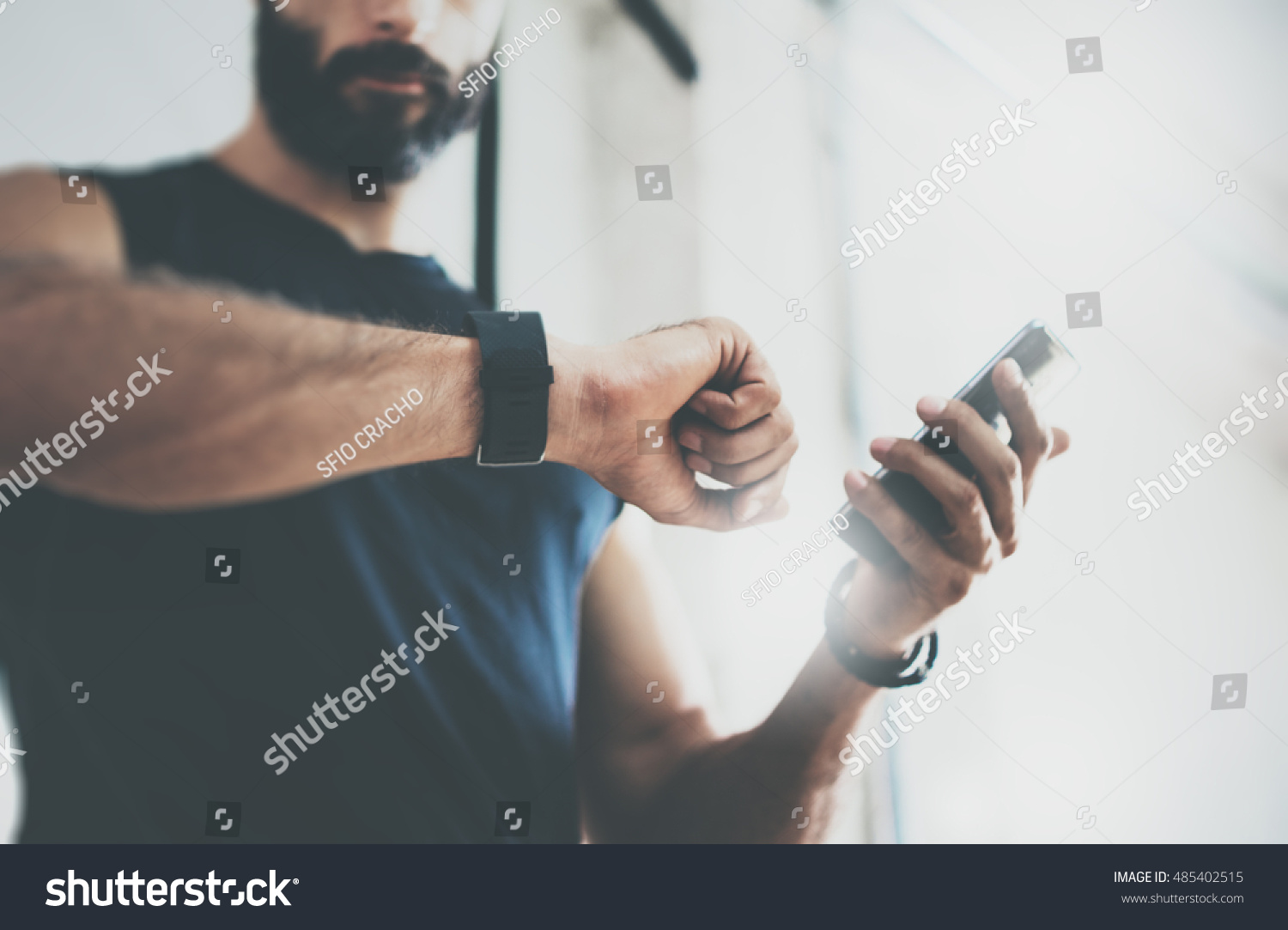 Close-up Shot Bearded Sportive Man After Workout Session Checks Fitness Results Smartphone.Adult Guy Wearing Sport Tracker Wristband Arm.Training hard inside gym.Horizontal bar background.Blurred #485402515