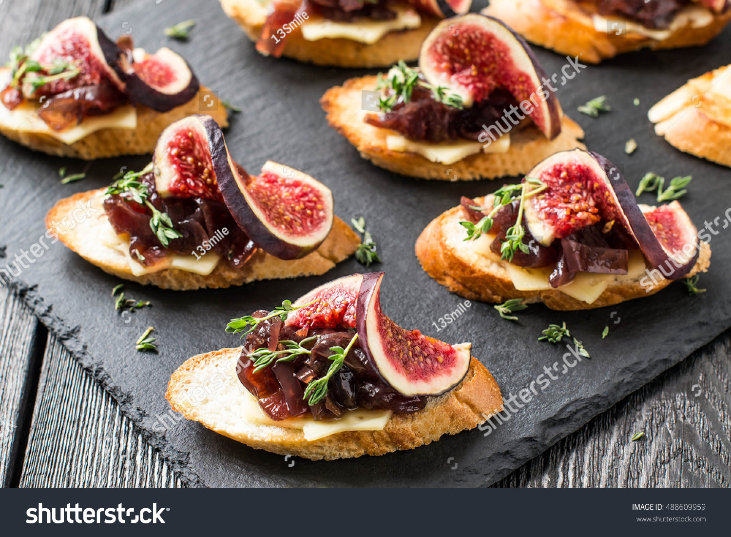 Canape or crostini with toasted baguette, cheese, onion jam, figs and fresh thyme on a slate board. Delicious appetizer, ideal as an aperitif. Selective focus #488609959