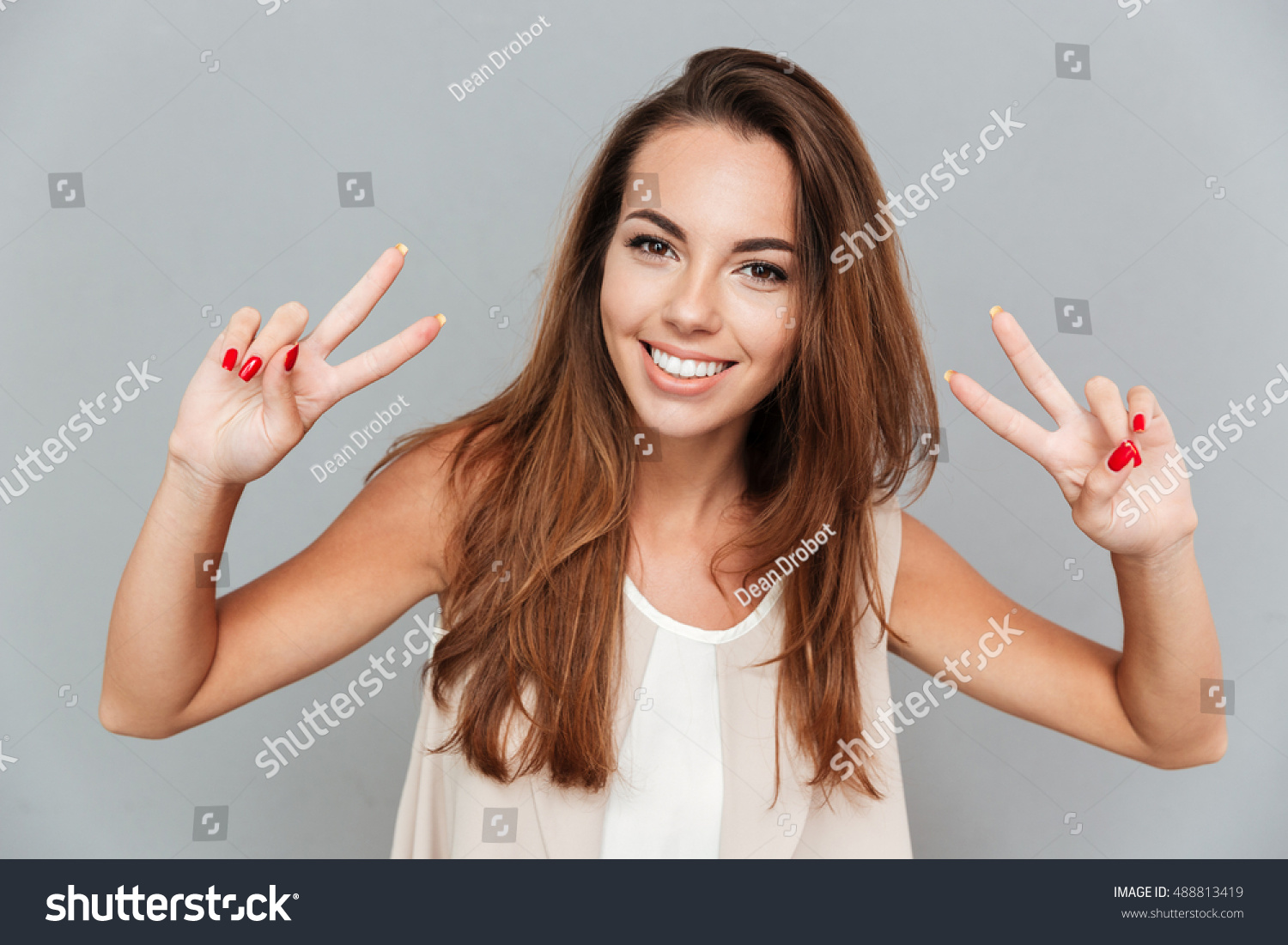 Happy beautiful young woman showing peace sign with both hands over grey background #488813419