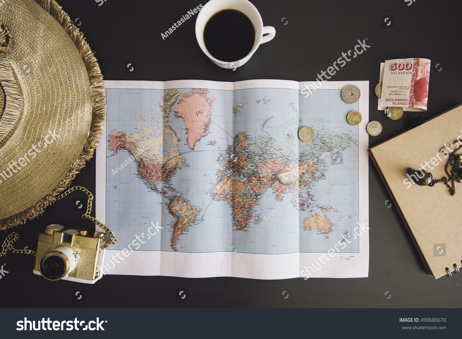 Planning the trip. World map with the hat, film camera, some money, notebook from recycled paper and freshly brewed coffee cup on the dark wooden table background. #490680670