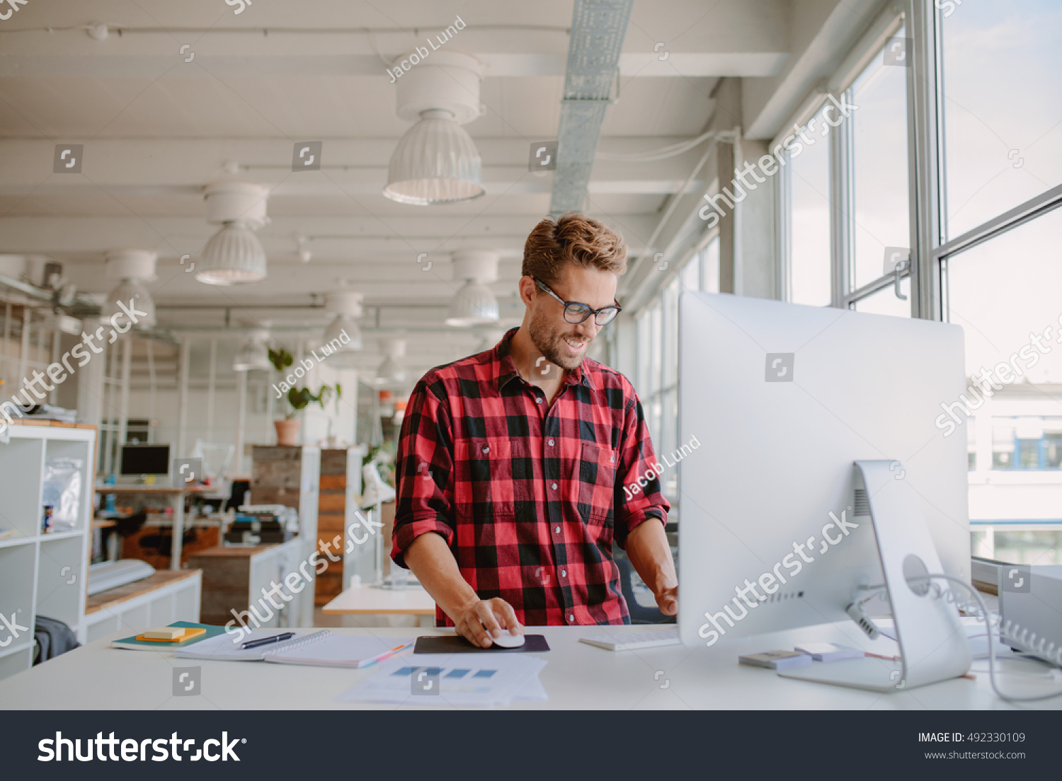 Shot of happy young man working on desktop computer in modern workplace. Young entrepreneur working at start up. #492330109