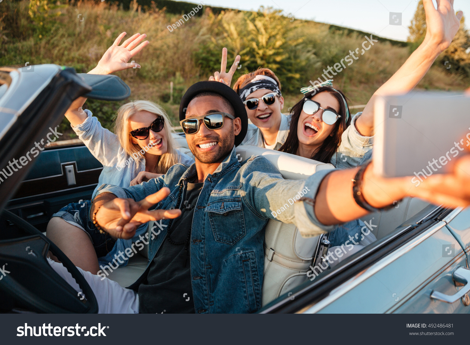 Multiethnic group of happy young people taking selfie with smartphone and showing peace sign in the car #492486481