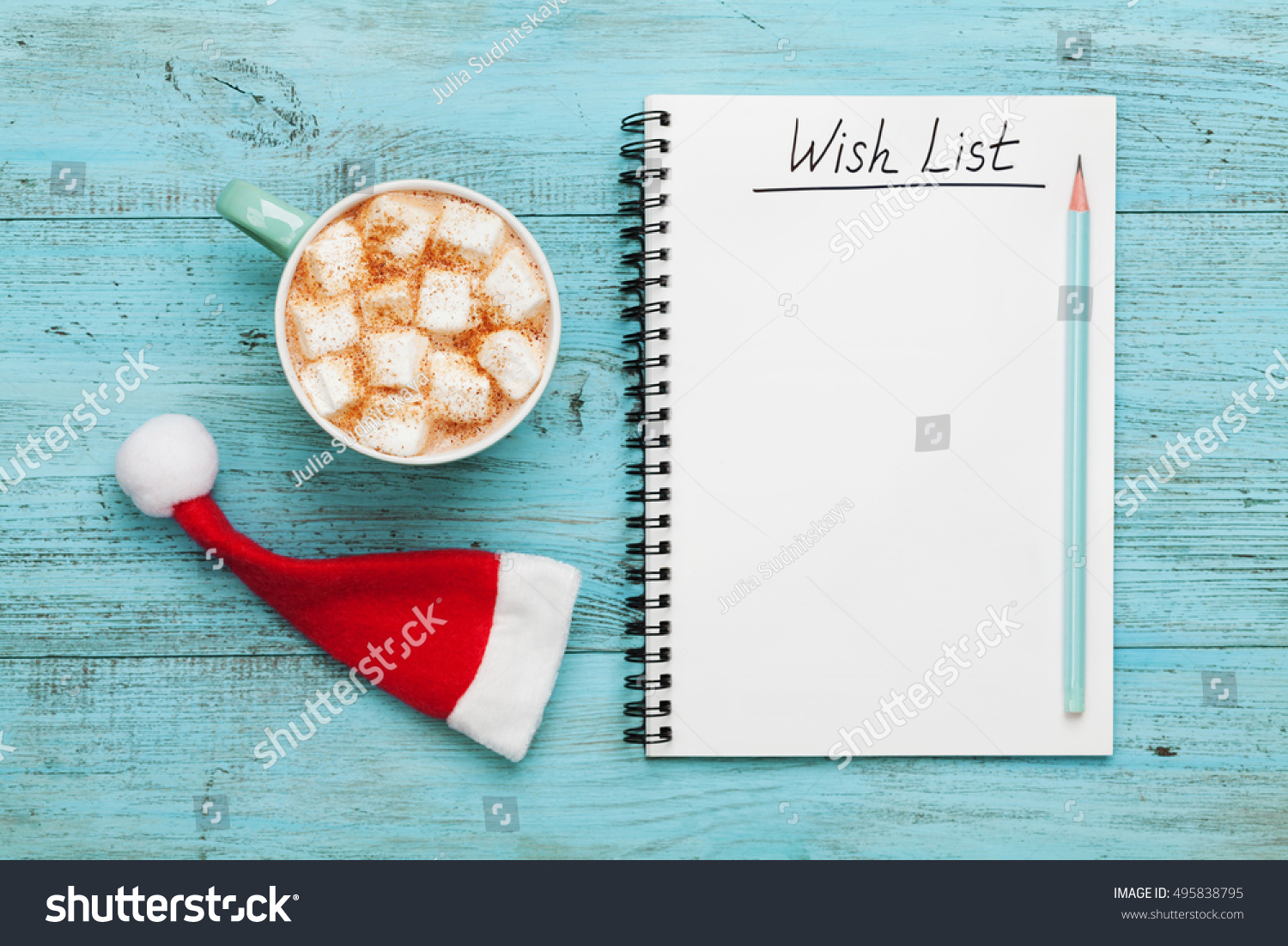 Cup of hot cocoa or chocolate with marshmallow, Santa Claus hat and notebook with wish list on turquoise vintage table from above, christmas planning concept. Flat lay. style.  #495838795