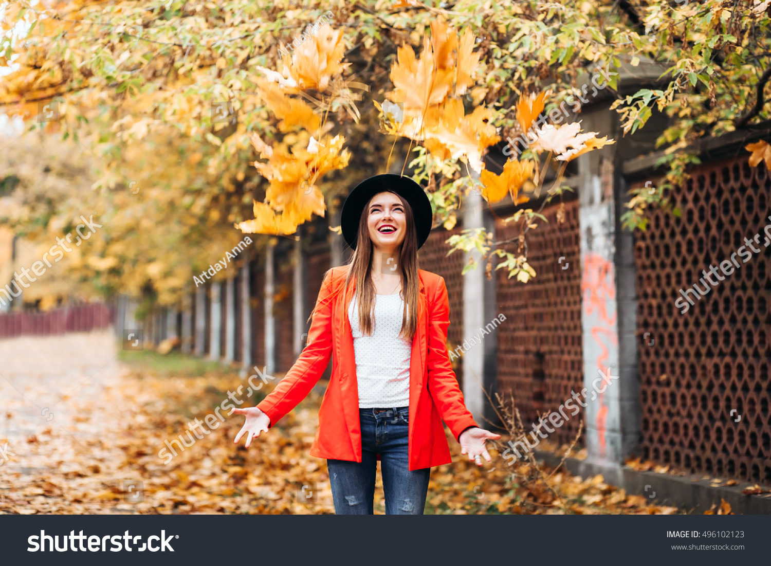 Happy young woman in red jacket and black hat throwing leaves and smiling on colorful nature city background, autumn

 #496102123