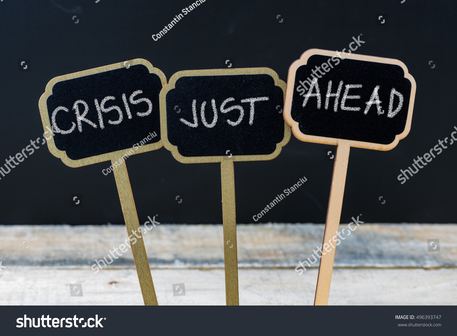 Business message CRISIS JUST AHEAD written with chalk on wooden mini blackboard labels, defocused chalkboard and wood table in background #496393747