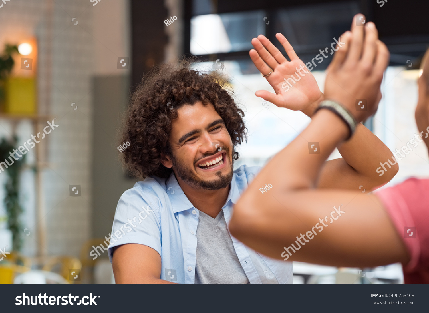 Portrait of friends giving high five at cafe while having lunch. Young guys friends giving a high five, slapping each others hand in congratulations while sitting in cafeteria. #496753468