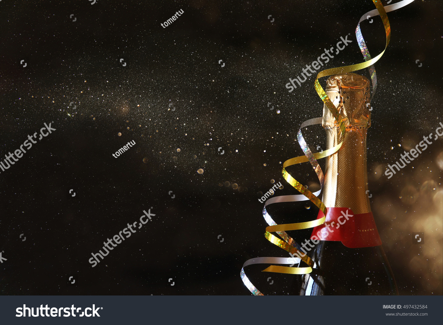 Champagne bottle in front of black background with glitter overlay. New year and celebration concept #497432584