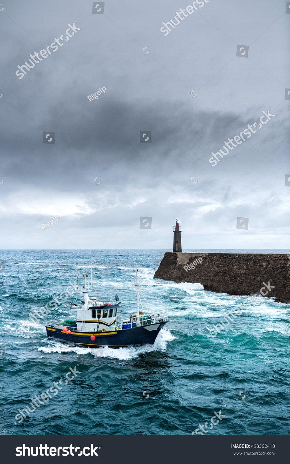 Fishing vessel under storm arriving at pier. 
It's a boat or ship used to catch fish in the sea. Fishing can be affected by storms.
Storms implies conditions like strong wind, precipitations or rain. #498362413