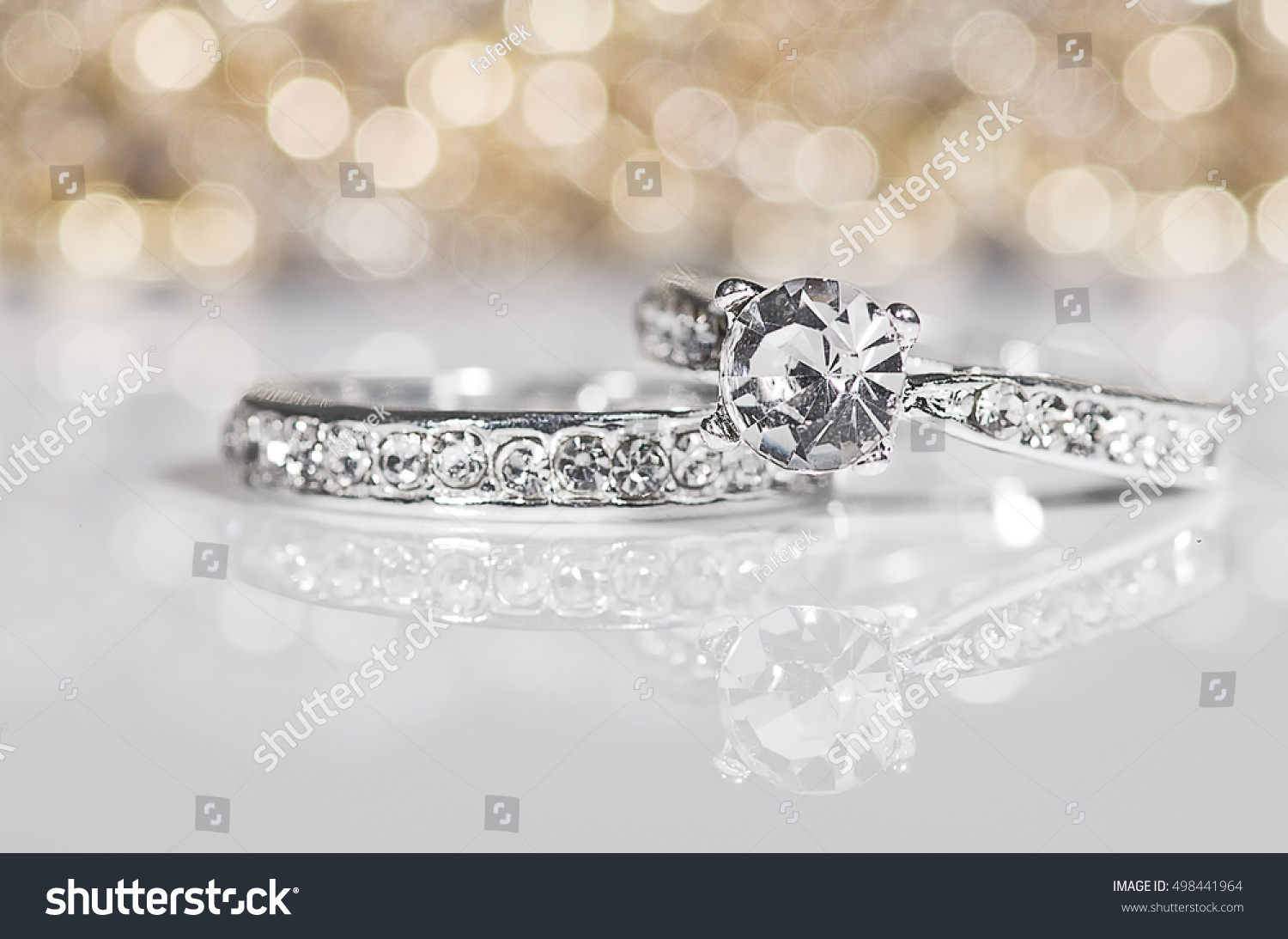 Silver Rings with diamonds on the white surface with golden reflections in the background. #498441964