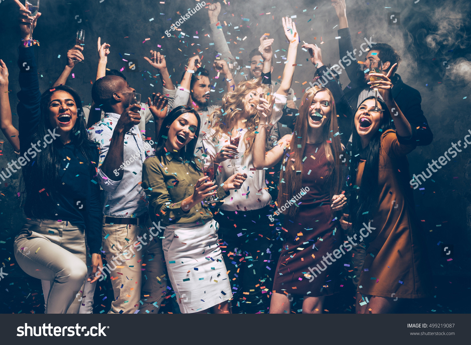 Party fun. Group of beautiful young people throwing colorful confetti and looking happy #499219087