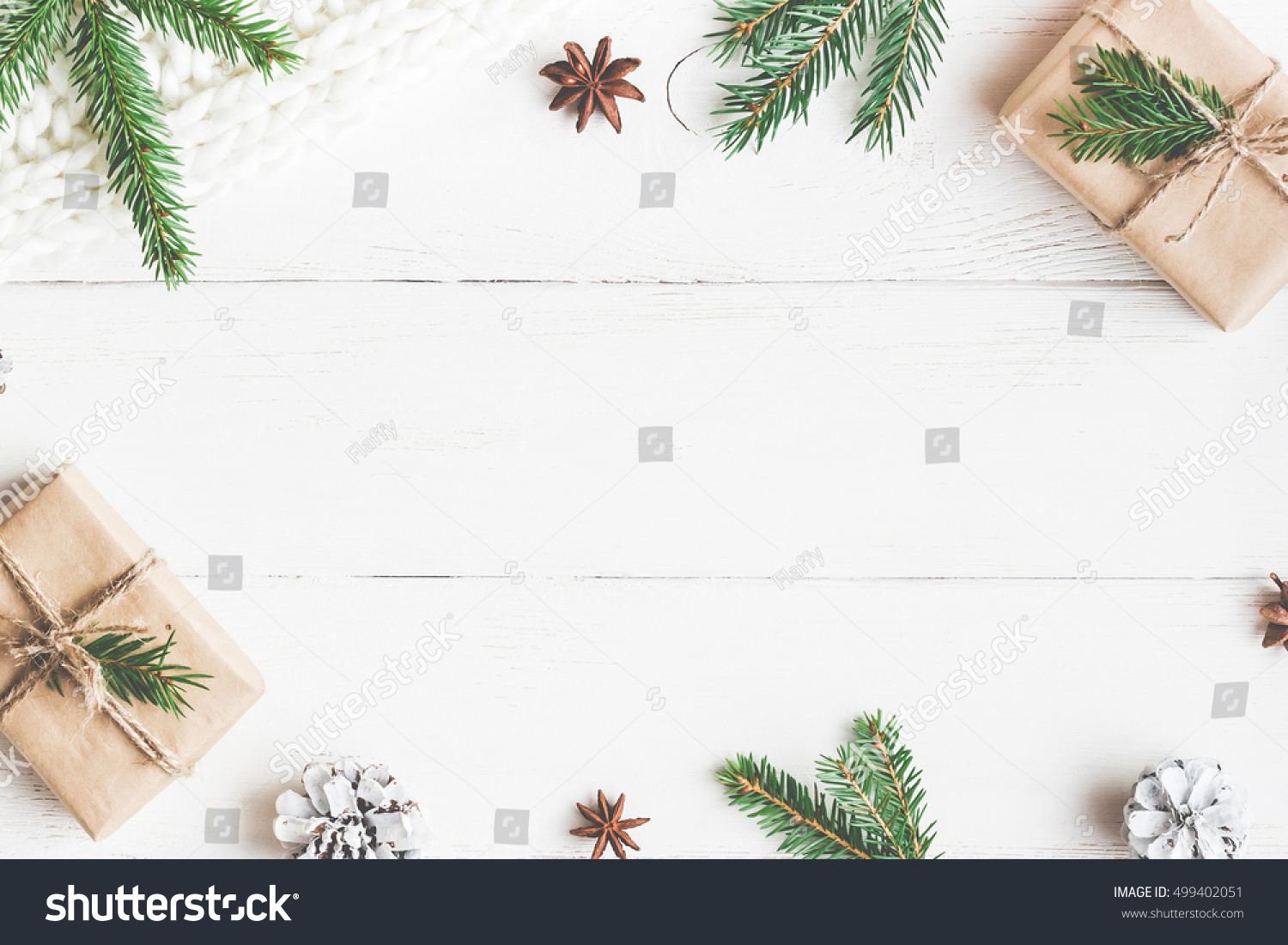 Christmas composition. Christmas gift, knitted blanket, pine cones, fir branches on wooden white background. Flat lay, top view, copy space #499402051