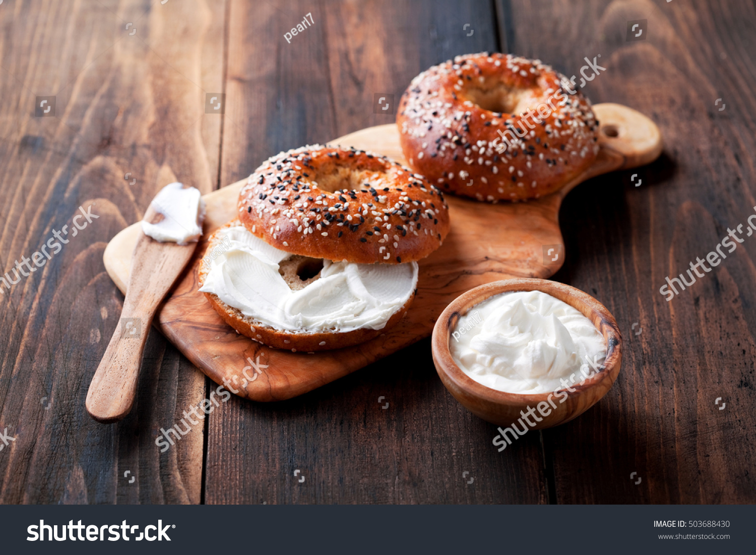 Whole grain bagels with cream cheese on wooden board, selective focus #503688430