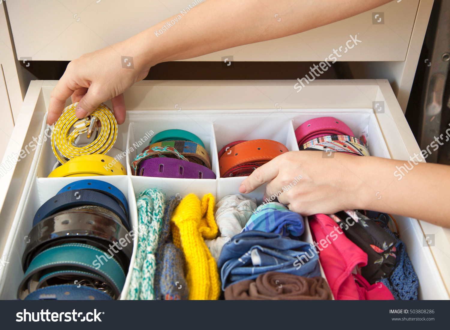The woman pulls out a strap from a drawer of the wardrobe. Drawer with straps and belts. #503808286