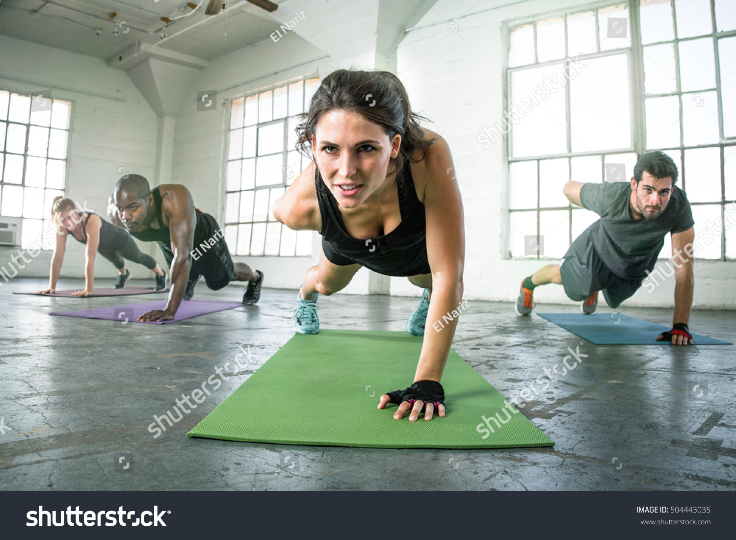 Strong powerful intense fit female leader of athletic fitness team exercising one arm push ups #504443035