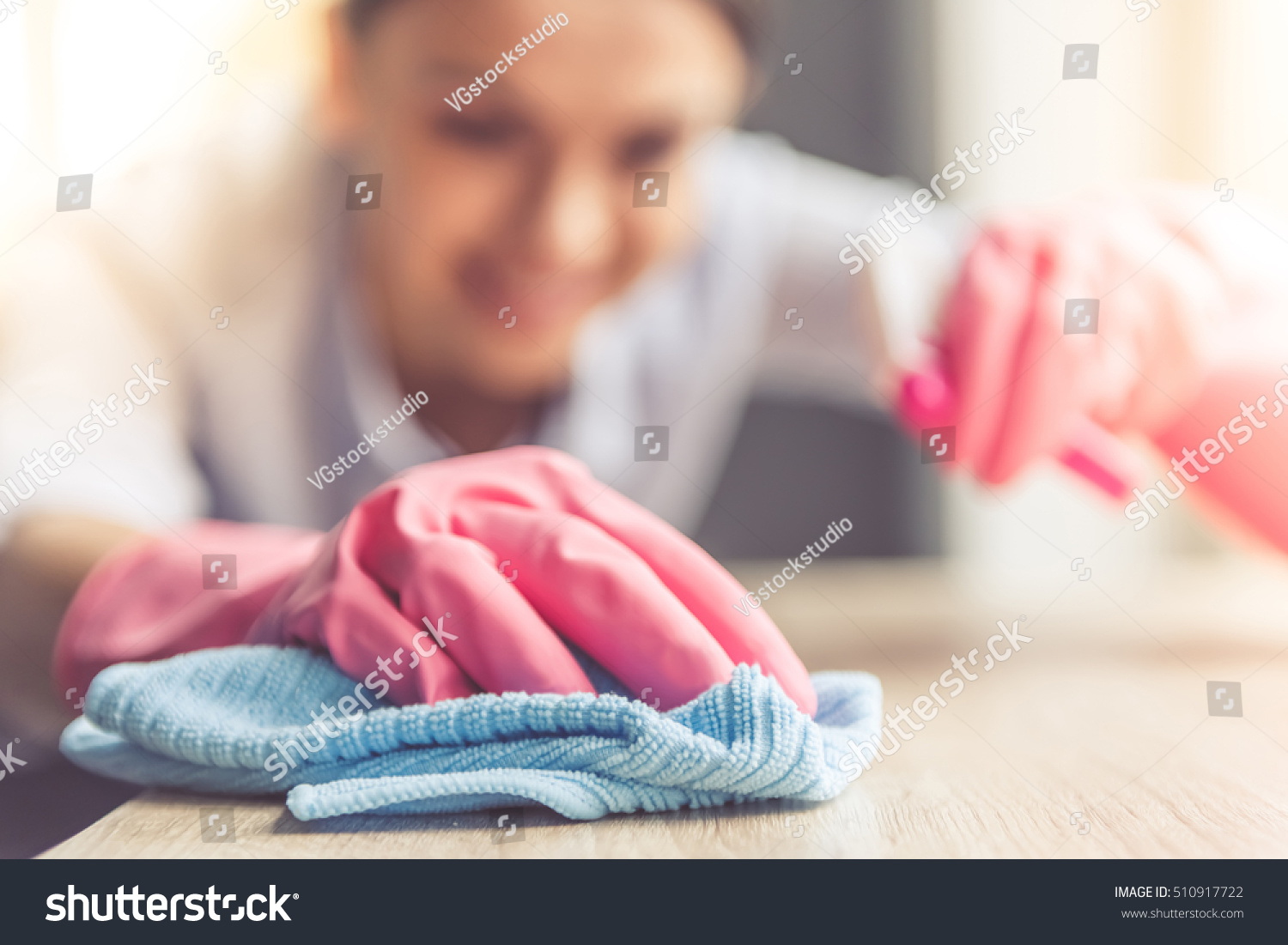 Woman in protective gloves is smiling and wiping dust using a spray and a duster while cleaning her house, close-up #510917722