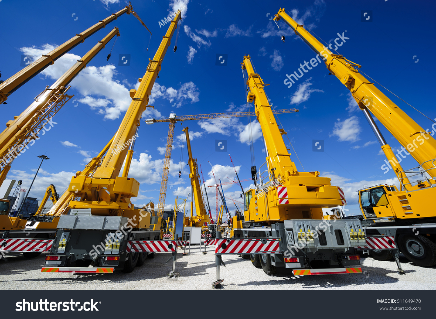 Mobile construction cranes with yellow telescopic arms and big tower cranes in sunny day with white clouds and deep blue sky on background, heavy industry  #511649470