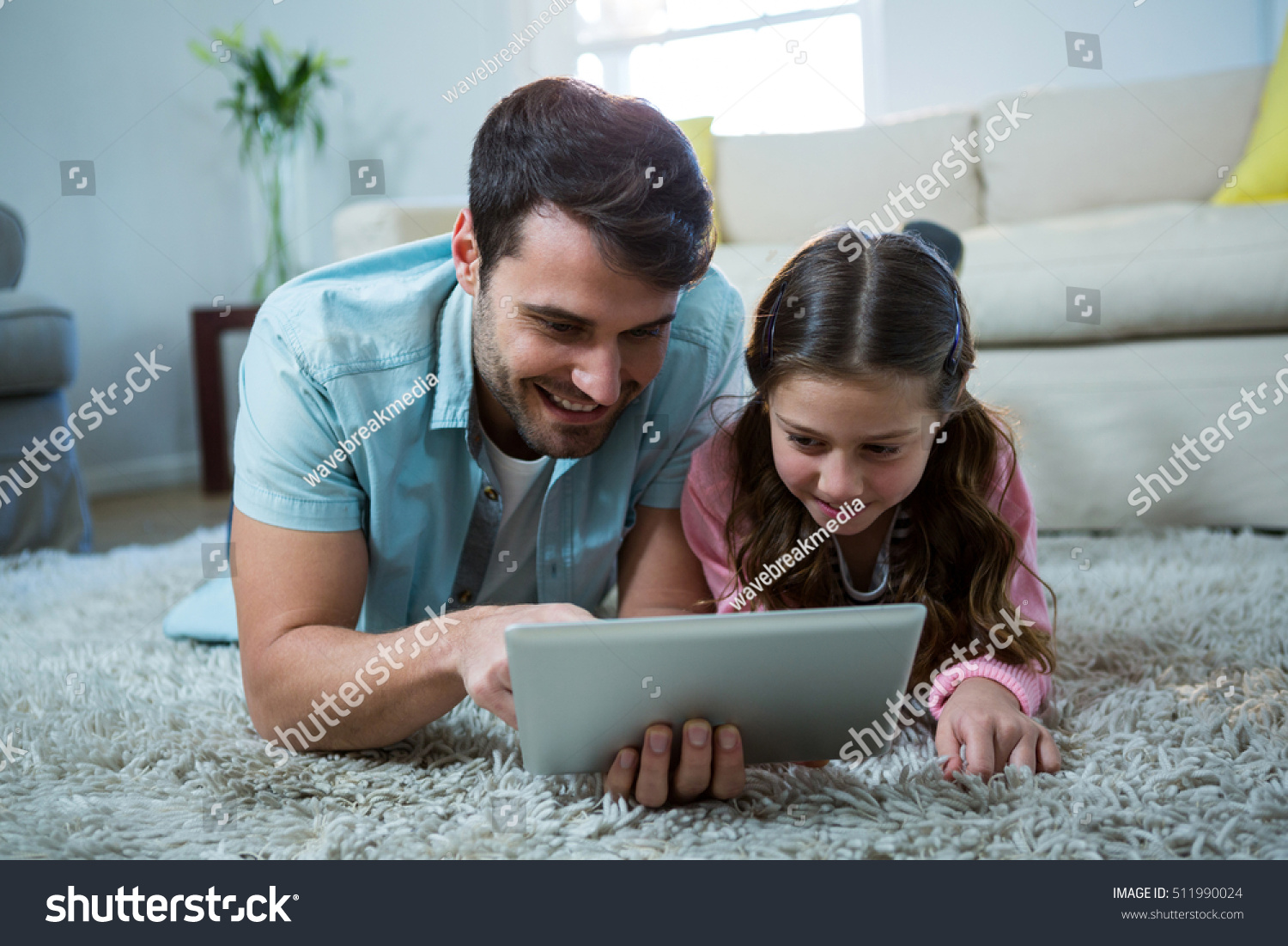 Father and daughter using digital tablet in the living room at home #511990024