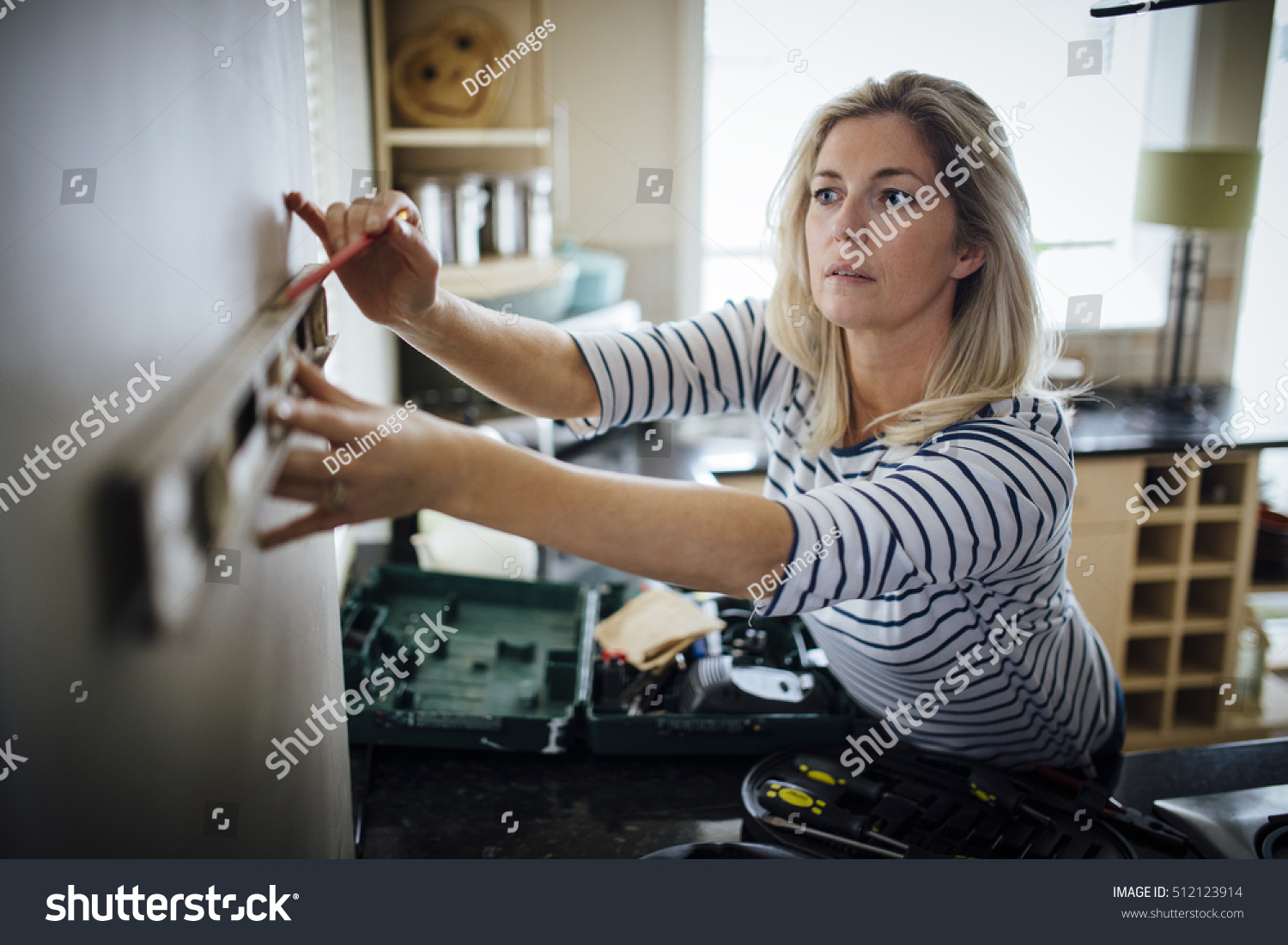 Mature woman using a spirit level and marking the wall with a pencil in her kitchen. #512123914