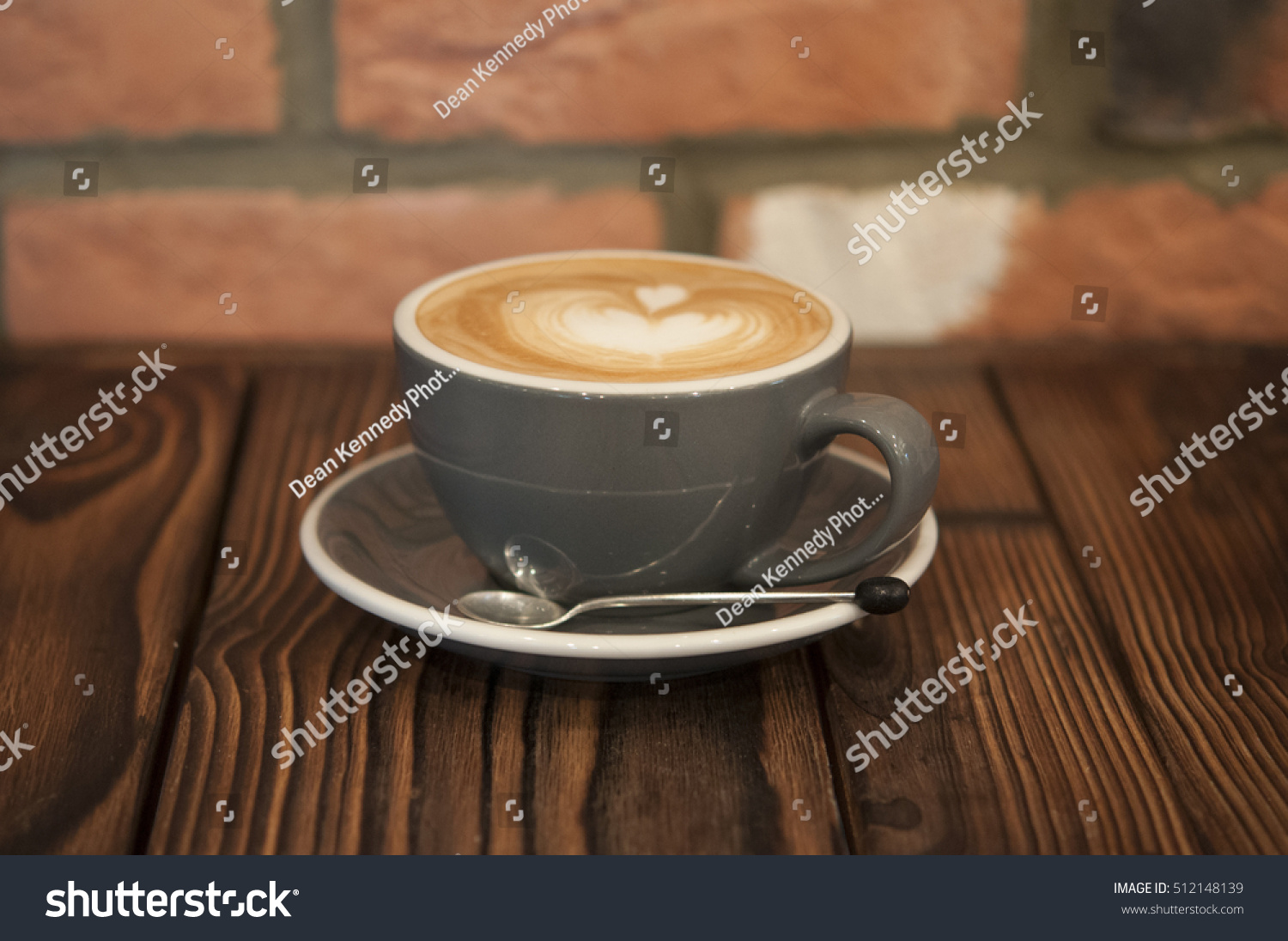 Photo of coffee in a cup, with a decorative design. Taken on wood with brick background #512148139