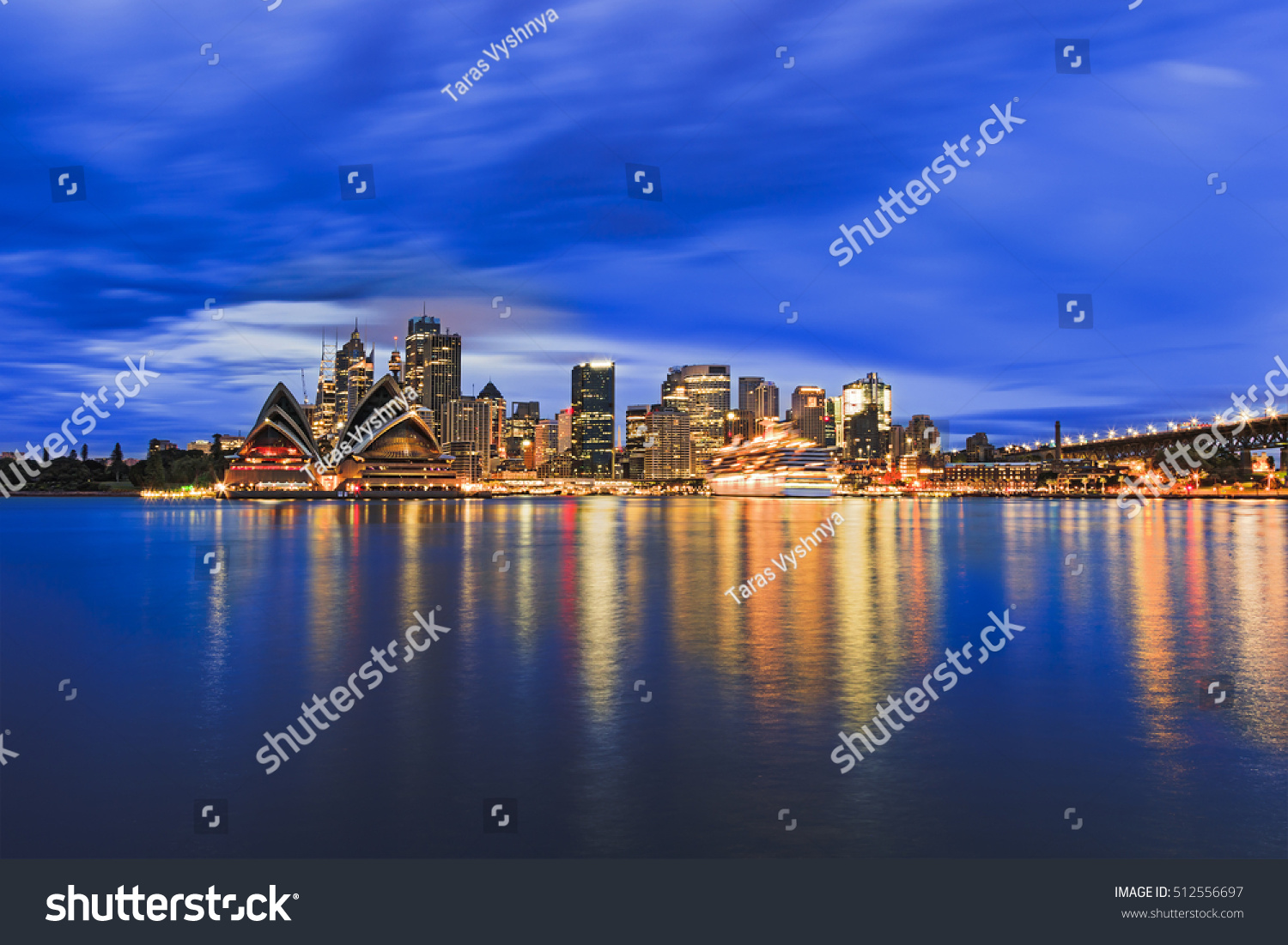 Sydney city CBD across Harbour blurred waters at sunrise when bright downtown lights reflect and blur between blue cloudy sky and flat water #512556697