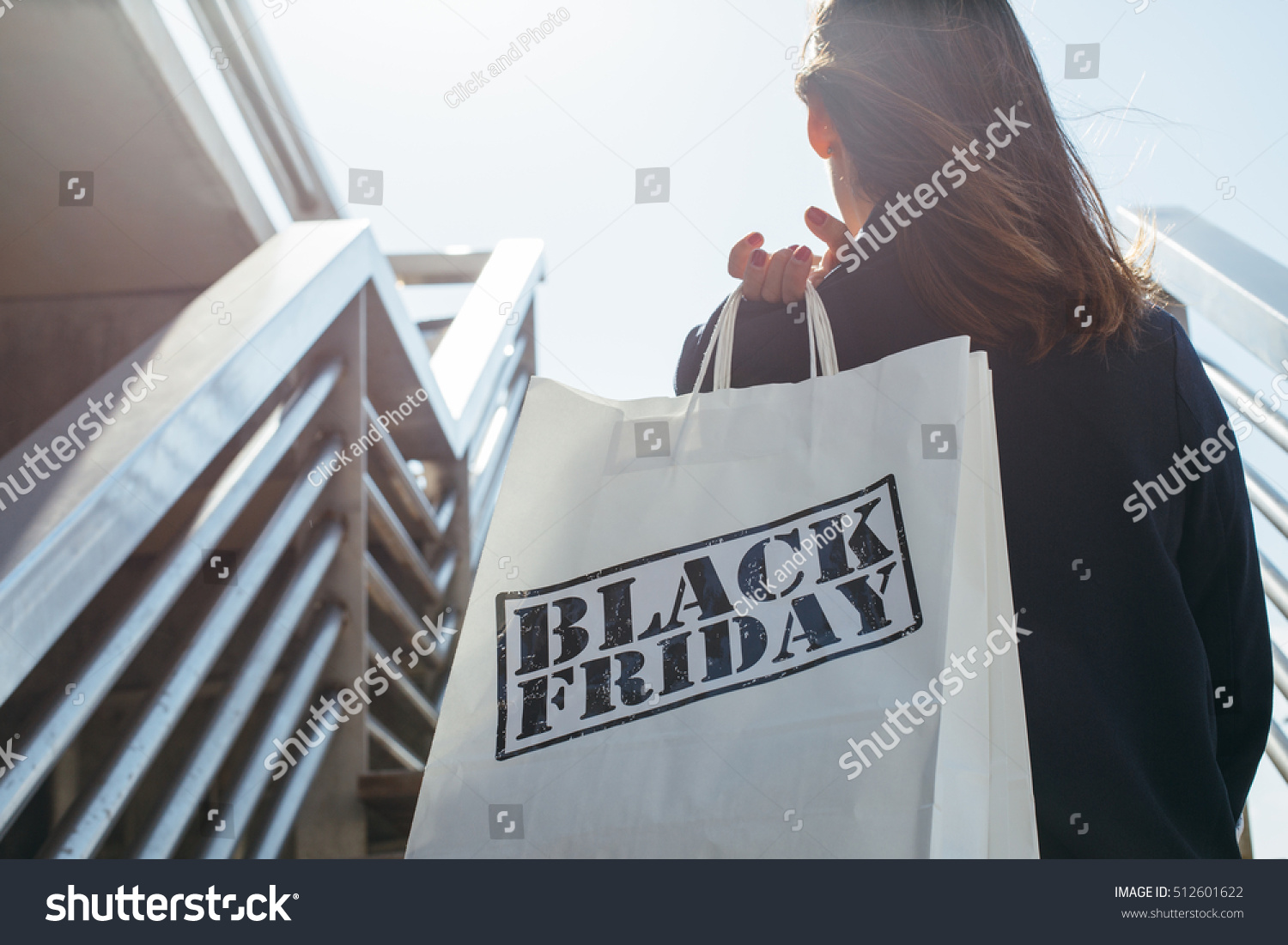 Rear view of incognito brunette holding Black Friday shopping bag while standing outdoors. Copy space #512601622