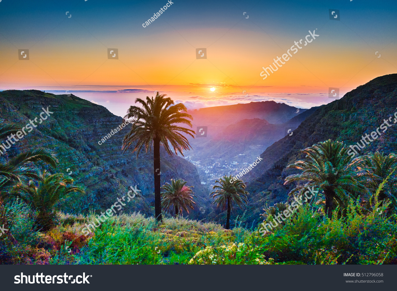Beautiful view of amazing tropical scenery with exotic palm trees and mountain valleys above wide open sea in golden evening light at sunset with blue sky and clouds in summer, Canary Islands, Spain #512796058