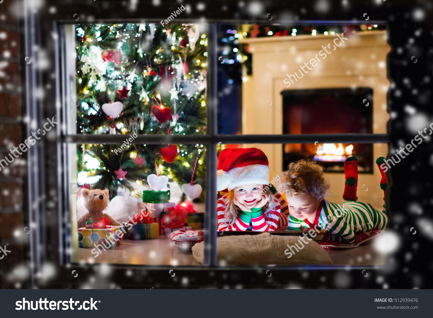 Happy little kids in matching red and green striped pajamas decorate Christmas tree in beautiful living room with traditional fire place. Children opening presents on Xmas eve. #512939476