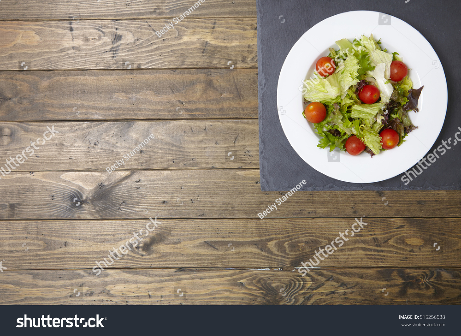 A bowl of fresh garden salad on a rustic wooden table top background, with empty space at side #515256538
